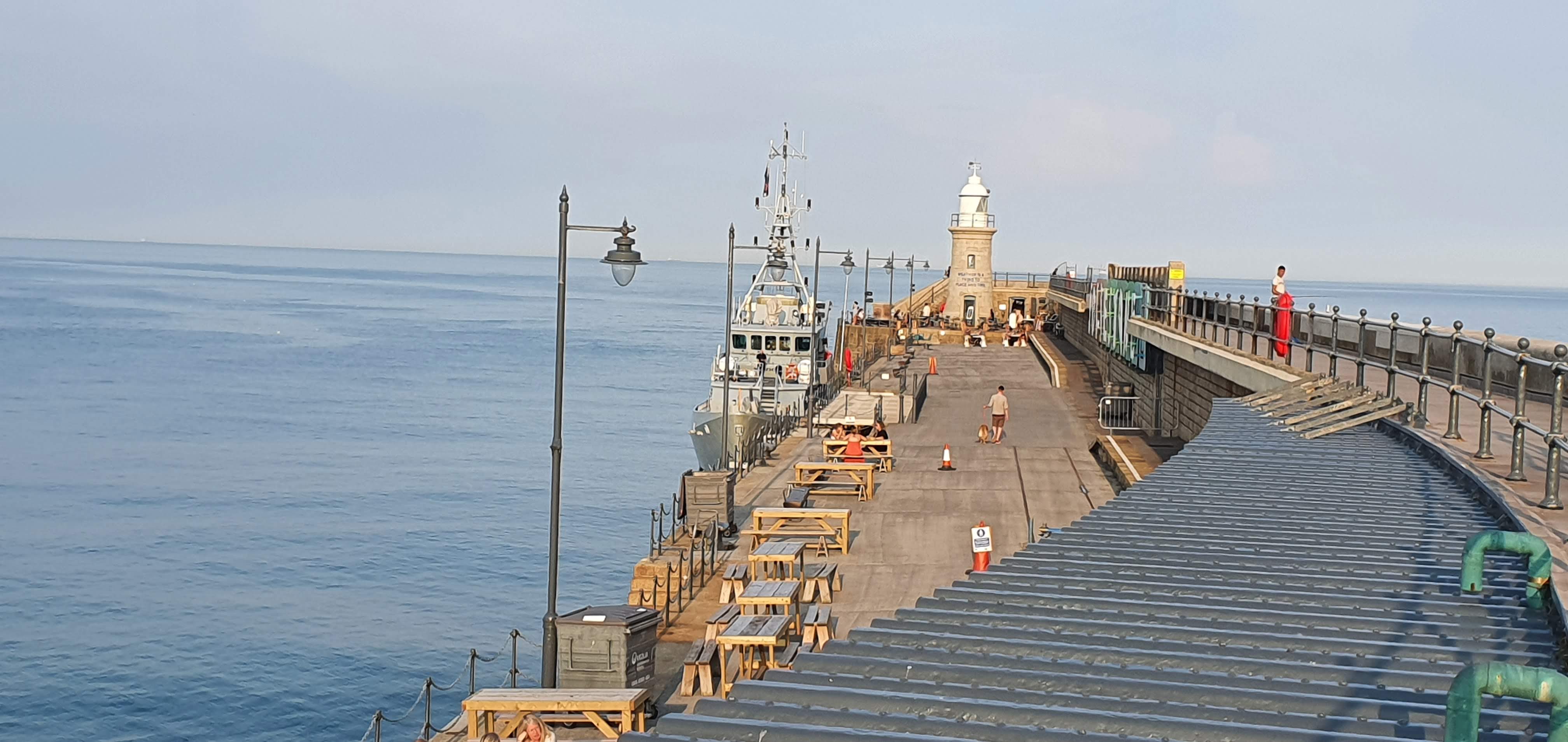Picture of the full lenght of the harbour arm with Lighthouse and a vessel